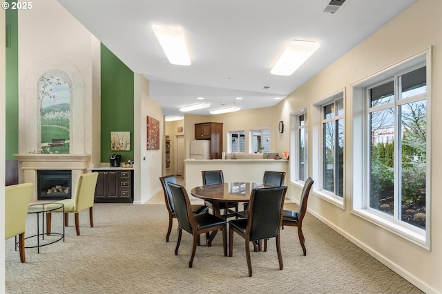 dining space with light carpet, a large fireplace, visible vents, and baseboards