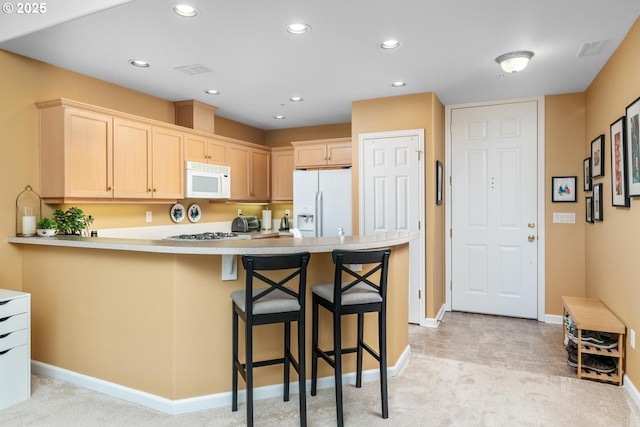 kitchen featuring white appliances, a peninsula, light countertops, a kitchen bar, and recessed lighting