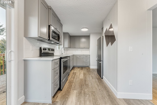 kitchen with tasteful backsplash, stainless steel appliances, light wood-type flooring, and gray cabinetry