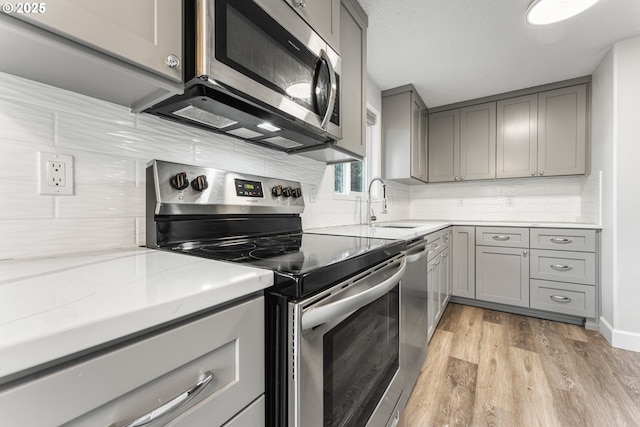 kitchen featuring sink, gray cabinetry, stainless steel appliances, tasteful backsplash, and light hardwood / wood-style floors