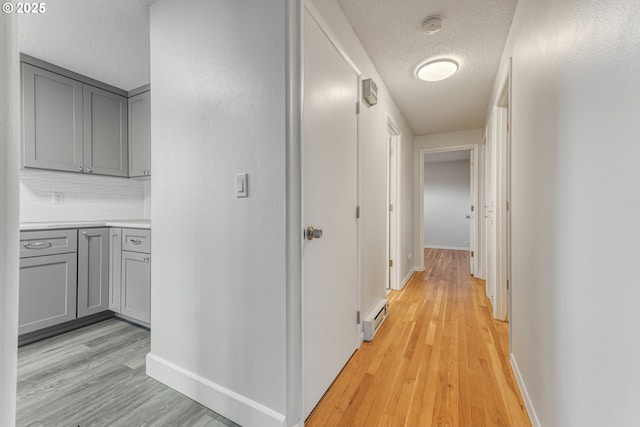 hallway with a baseboard heating unit, a textured ceiling, and light hardwood / wood-style floors