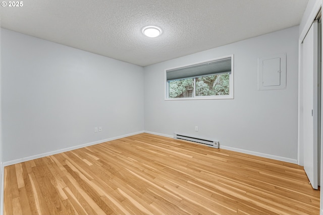 empty room with a baseboard heating unit, a textured ceiling, and light hardwood / wood-style flooring