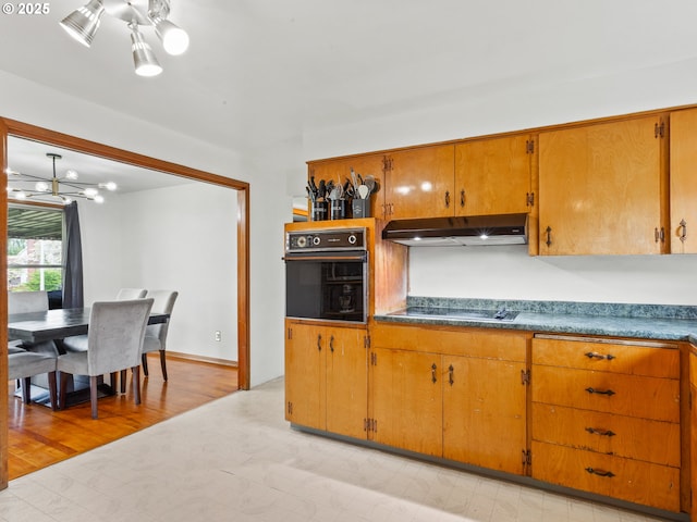 kitchen with under cabinet range hood, brown cabinets, a chandelier, and black appliances