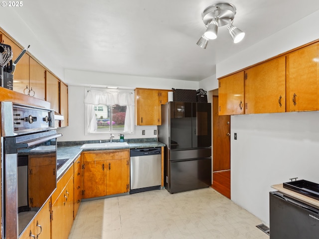 kitchen with brown cabinets, appliances with stainless steel finishes, a sink, and light floors