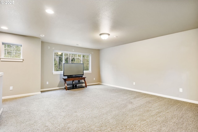 unfurnished living room featuring a wealth of natural light, a textured ceiling, baseboards, and carpet floors