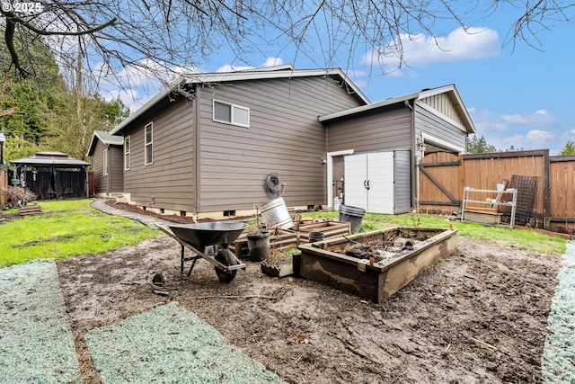 rear view of house featuring an outbuilding, a gate, fence, a yard, and a vegetable garden