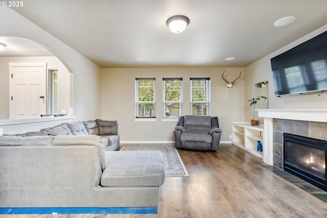 living room with baseboards, arched walkways, wood finished floors, and a tiled fireplace