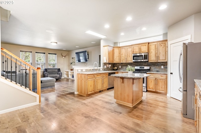 kitchen with light wood-style flooring, backsplash, open floor plan, a center island, and appliances with stainless steel finishes