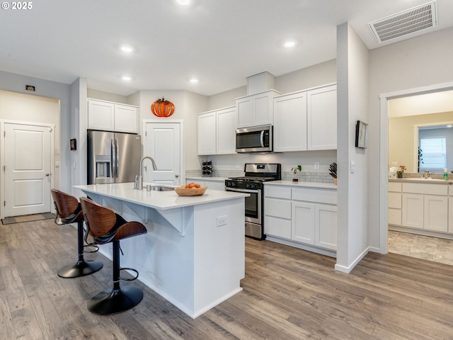 kitchen with a breakfast bar, sink, a center island with sink, stainless steel appliances, and white cabinets