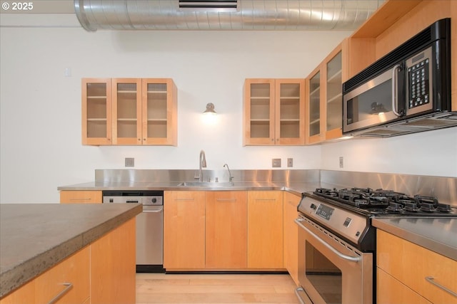 kitchen with appliances with stainless steel finishes, sink, stainless steel counters, light brown cabinets, and light hardwood / wood-style flooring