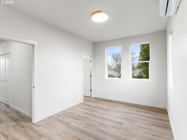 empty room featuring baseboards, an AC wall unit, and light wood finished floors