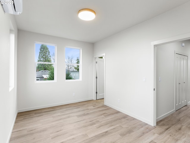 spare room with baseboards, light wood-style floors, and a wall mounted AC