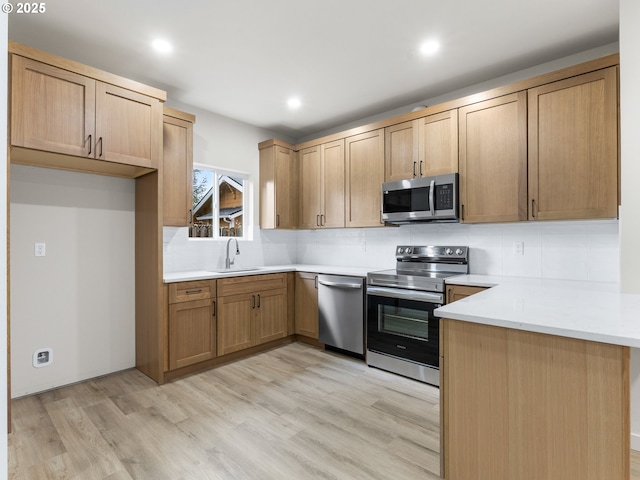 kitchen featuring light wood finished floors, tasteful backsplash, a peninsula, stainless steel appliances, and a sink