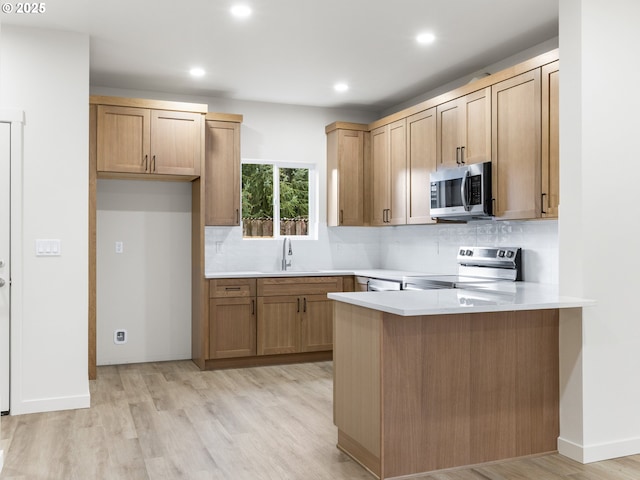 kitchen featuring a peninsula, light wood-style flooring, a sink, appliances with stainless steel finishes, and backsplash