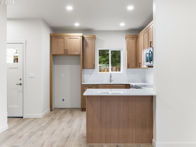 kitchen featuring light wood-style flooring, a sink, stainless steel microwave, tasteful backsplash, and a peninsula