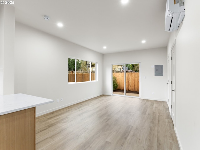 spare room with baseboards, an AC wall unit, light wood-type flooring, electric panel, and recessed lighting