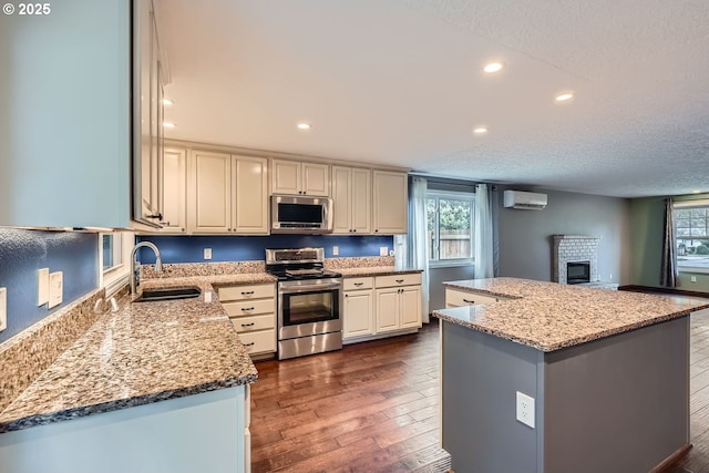 kitchen featuring appliances with stainless steel finishes, light stone countertops, dark hardwood / wood-style floors, a kitchen island, and sink