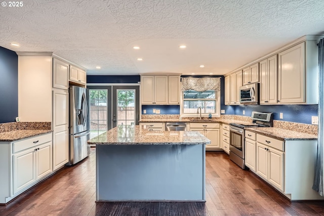 kitchen featuring light stone countertops, dark hardwood / wood-style flooring, a center island, and appliances with stainless steel finishes