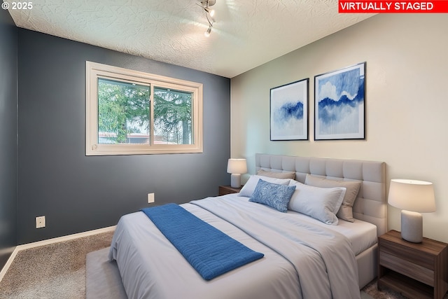 carpeted bedroom featuring track lighting and a textured ceiling