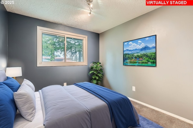 bedroom featuring rail lighting, a textured ceiling, and carpet floors