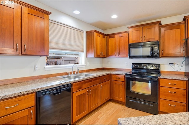 kitchen featuring brown cabinets, a sink, light stone countertops, light wood-type flooring, and black appliances