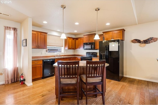 kitchen featuring a center island, a breakfast bar area, hanging light fixtures, light wood-style flooring, and black appliances