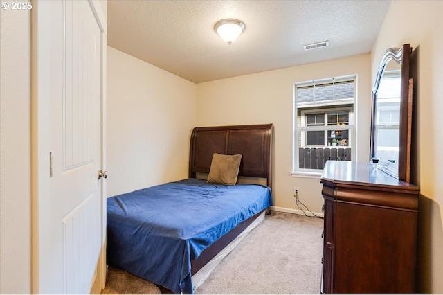 bedroom featuring light carpet, baseboards, visible vents, and a textured ceiling