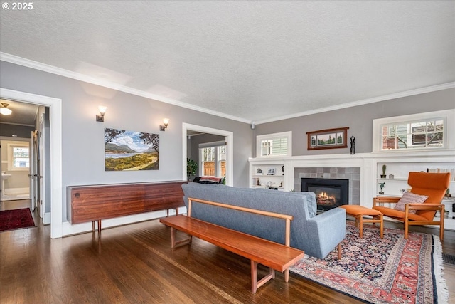 living room with a wealth of natural light, ornamental molding, a tiled fireplace, a textured ceiling, and wood finished floors