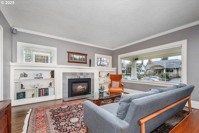 living area featuring a tiled fireplace, a textured ceiling, wood finished floors, crown molding, and baseboards