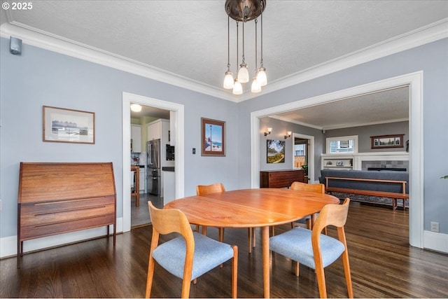 dining space featuring crown molding, baseboards, a tile fireplace, dark wood-style floors, and a textured ceiling