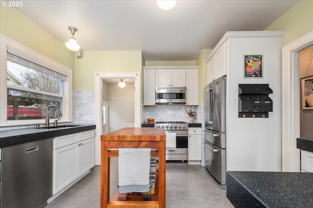 kitchen featuring dark stone counters, a sink, white cabinets, high quality appliances, and tasteful backsplash