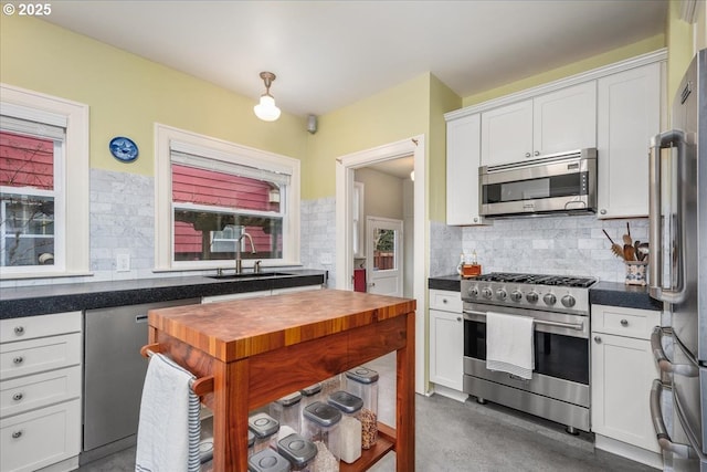 kitchen with a wealth of natural light, a sink, tasteful backsplash, white cabinetry, and appliances with stainless steel finishes