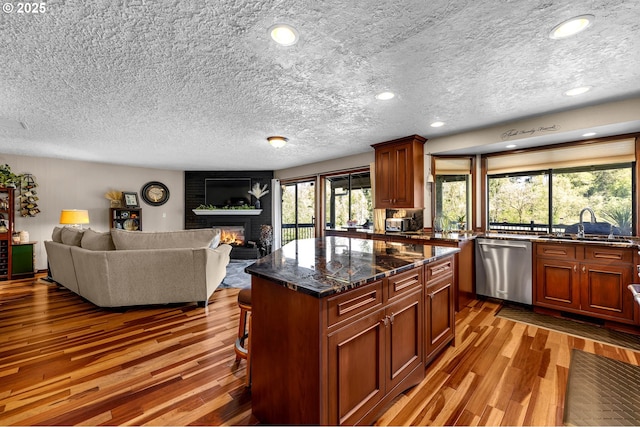 kitchen featuring dishwasher, wood finished floors, a sink, a brick fireplace, and a textured ceiling