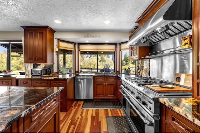kitchen featuring stainless steel appliances, extractor fan, a textured ceiling, light wood-style floors, and dark stone countertops