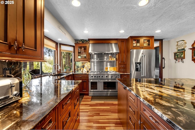 kitchen with high quality appliances, wall chimney range hood, a sink, a textured ceiling, and recessed lighting