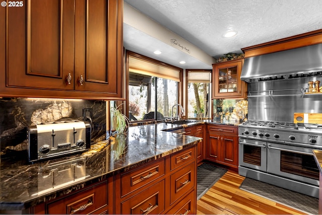 kitchen with double oven range, range hood, a textured ceiling, a sink, and light wood-style flooring