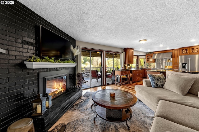 living room featuring a textured ceiling, light wood-style flooring, recessed lighting, and a brick fireplace