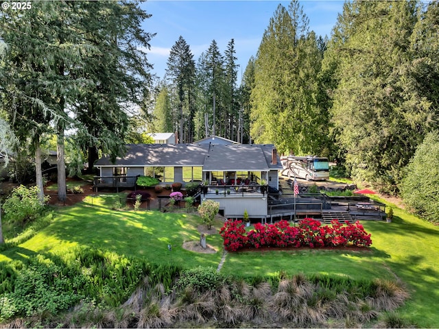 rear view of property featuring a wooden deck, a lawn, and a wooded view