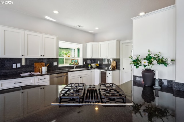 kitchen featuring stainless steel dishwasher, a sink, decorative backsplash, stovetop with downdraft, and white cabinets