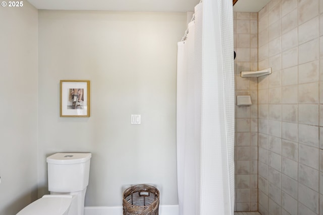 bathroom featuring toilet, baseboards, and a tile shower