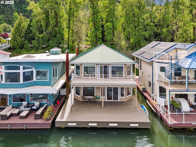rear view of house featuring a deck with water view, a wooded view, an outdoor living space, and a balcony