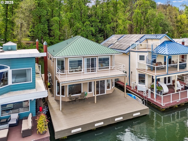 rear view of house featuring a wooded view, metal roof, a deck with water view, and a balcony