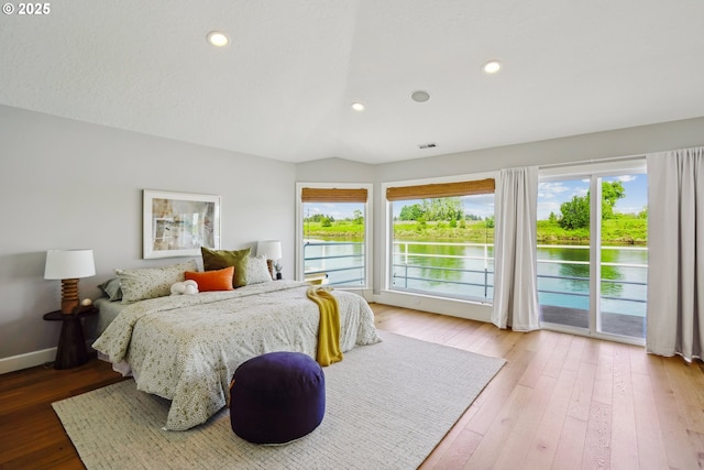 bedroom featuring a water view, multiple windows, access to outside, and lofted ceiling