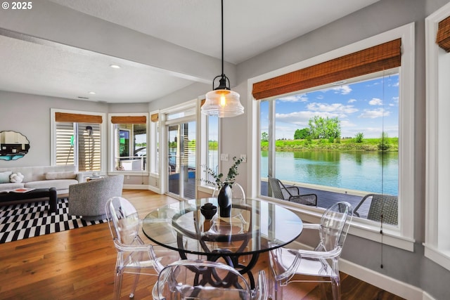 dining room with recessed lighting, a water view, baseboards, and wood finished floors