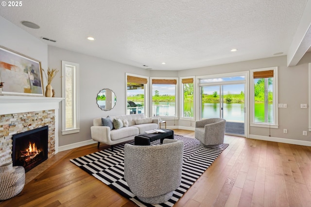 living room featuring a textured ceiling, wood-type flooring, a water view, baseboards, and a stone fireplace