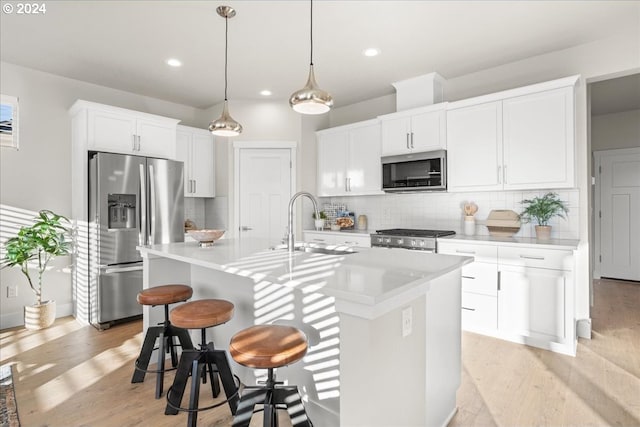 kitchen with stainless steel appliances, white cabinetry, a center island with sink, and backsplash