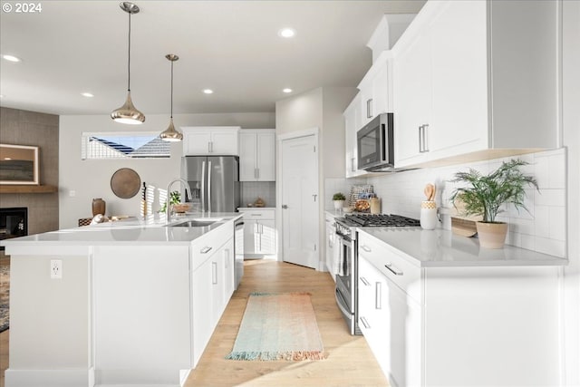 kitchen with white cabinetry, appliances with stainless steel finishes, light wood finished floors, a center island with sink, and pendant lighting