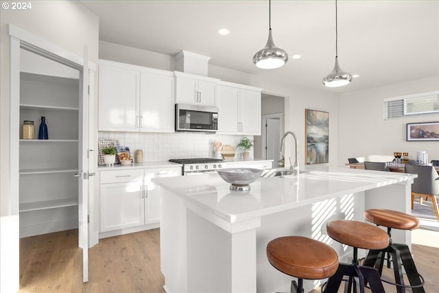 kitchen with sink, hanging light fixtures, a center island with sink, white cabinets, and stove