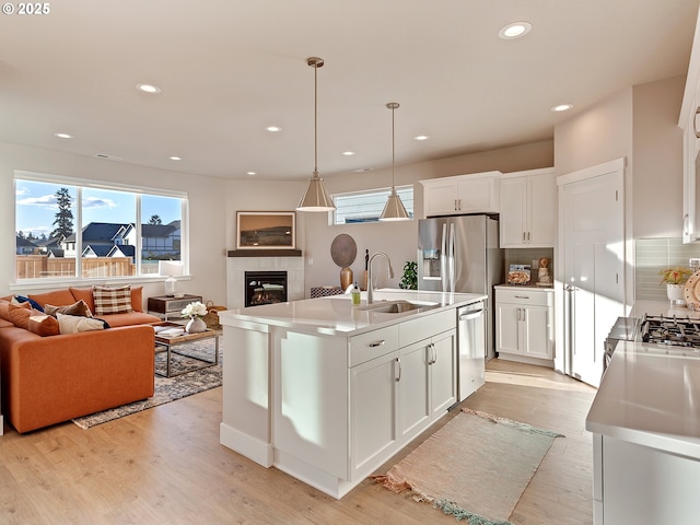 kitchen featuring stainless steel appliances, a tiled fireplace, light wood-style floors, white cabinetry, and a sink