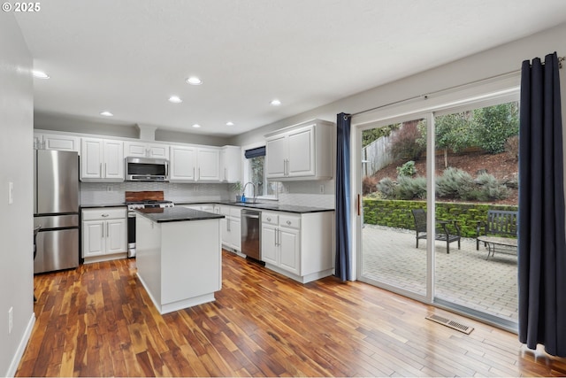 kitchen with stainless steel appliances, sink, white cabinetry, backsplash, and a kitchen island